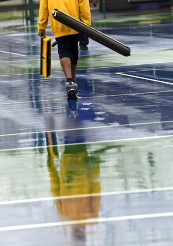 Reynoldsburg tennis player Camron Roark carries a broom and squeegee to the sideline prior to the teams soggy practice at the school on March 25.